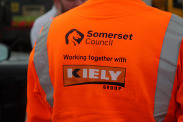 A person's back wearing a Somerset Council and Kiely Group orange Hi-Viz jacket.