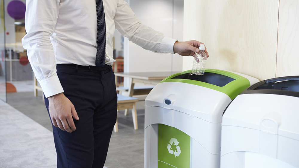 An office worker throwing a plastic bottle into a recycling bin.