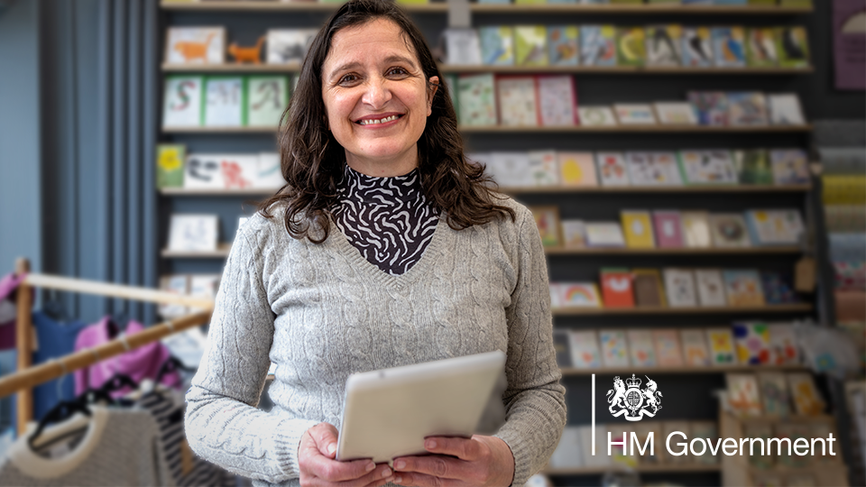 A smiling woman holding a tablet with a bookshelf in the background.