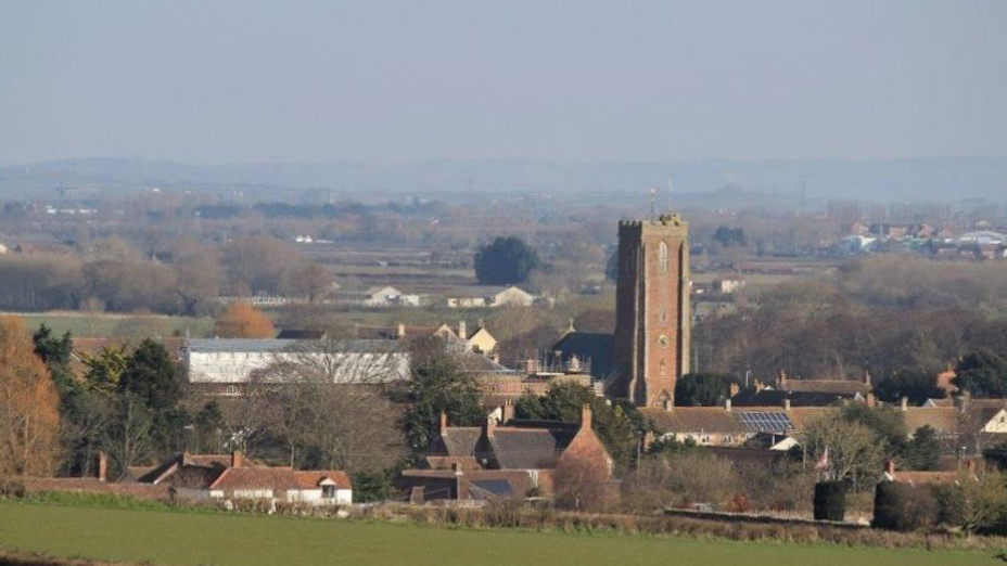 Landscape of Cannington on a sunny day with trees, houses, rolling fields and St. Mary’s Church as the focal point.