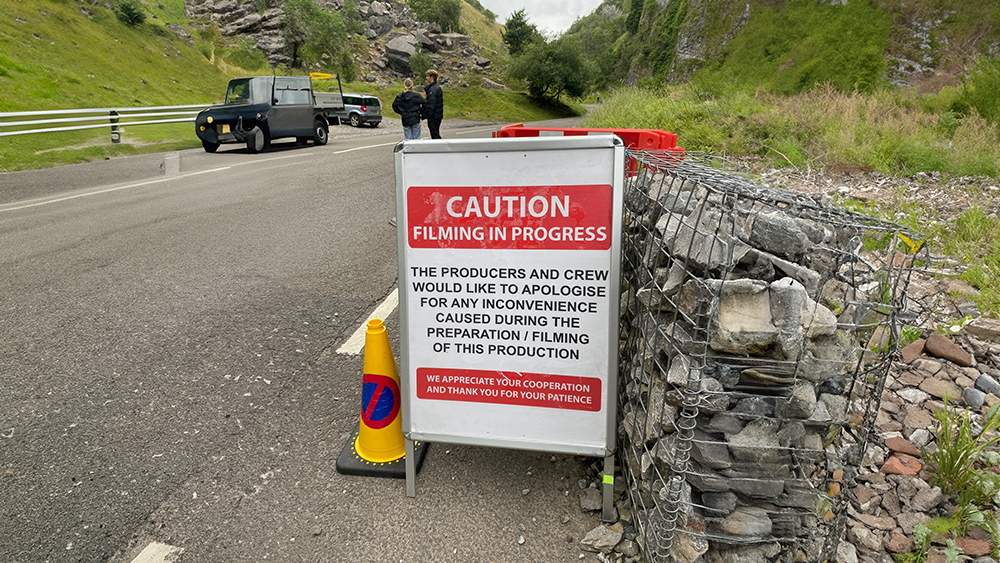 An A frame sign situated at Cheddar Gorge stating caution. filming in progress.