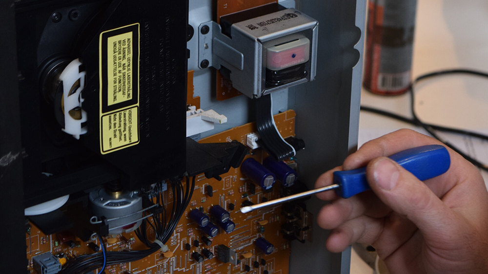 A hand holding a screwdriver repairing a opened DVD player.