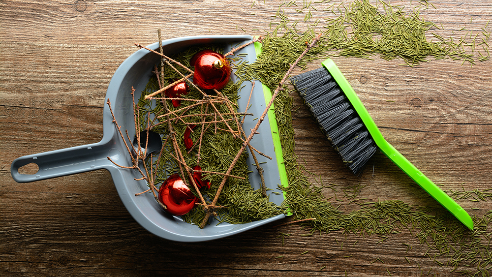 Dustpan and brush on a wooden floor used to sweep up baubles, twigs and pine needles.