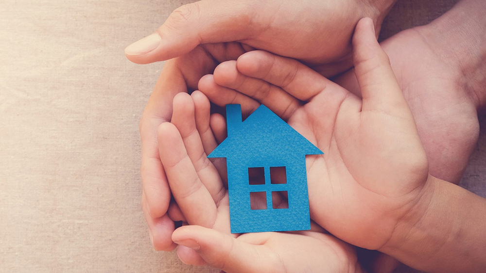 Adult and child's hands cupping a blue paper cut-out of a house.
