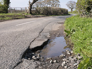 A large pothole on the side of a rural country road.