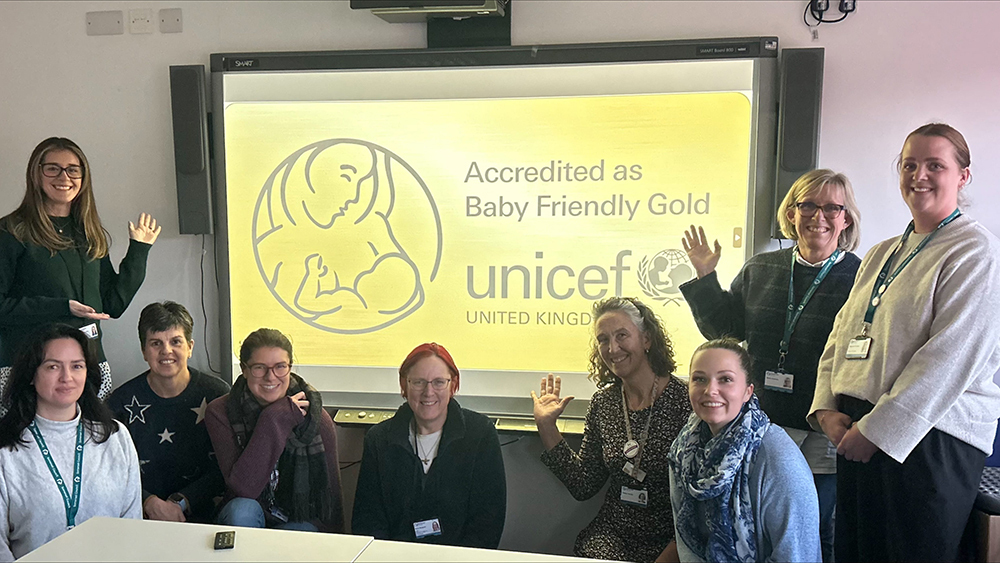 A group of all-female Somerset Health Visitors waving to the camera in front of a presentation screen.