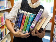 A woman holding a large stack of library books.