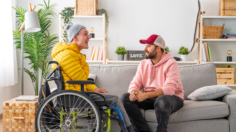 Disabled man in wheelchair and friends chatting relaxed in the living room of the house.