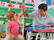 A child and preschool teacher high-fiving each other in a classroom.