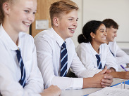 Line of secondary school students wearing uniforms sitting at their desks in a classroom.