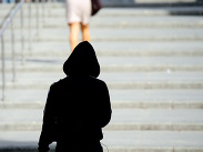 A woman being followed up a row of steps by a hooded figure.