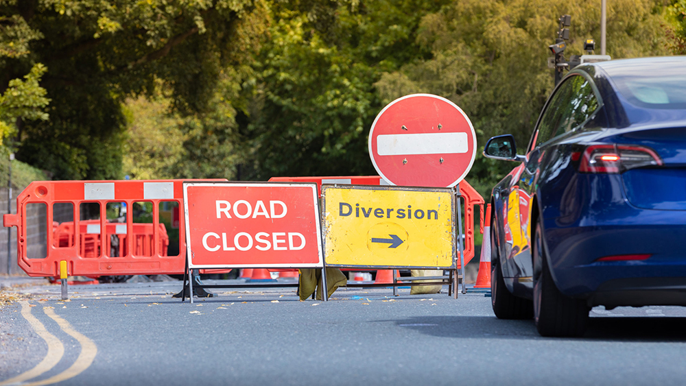 Traffic signs diverting a blue car around fenced-off road works.