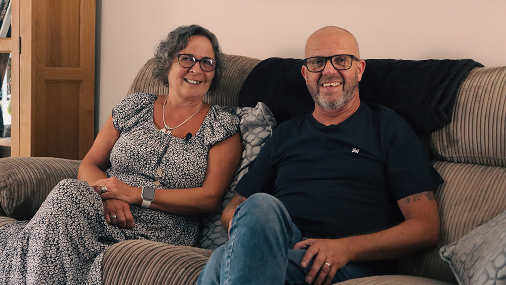 Foster parents Amanda and Steve, smiling whilst sat on their sofa.
