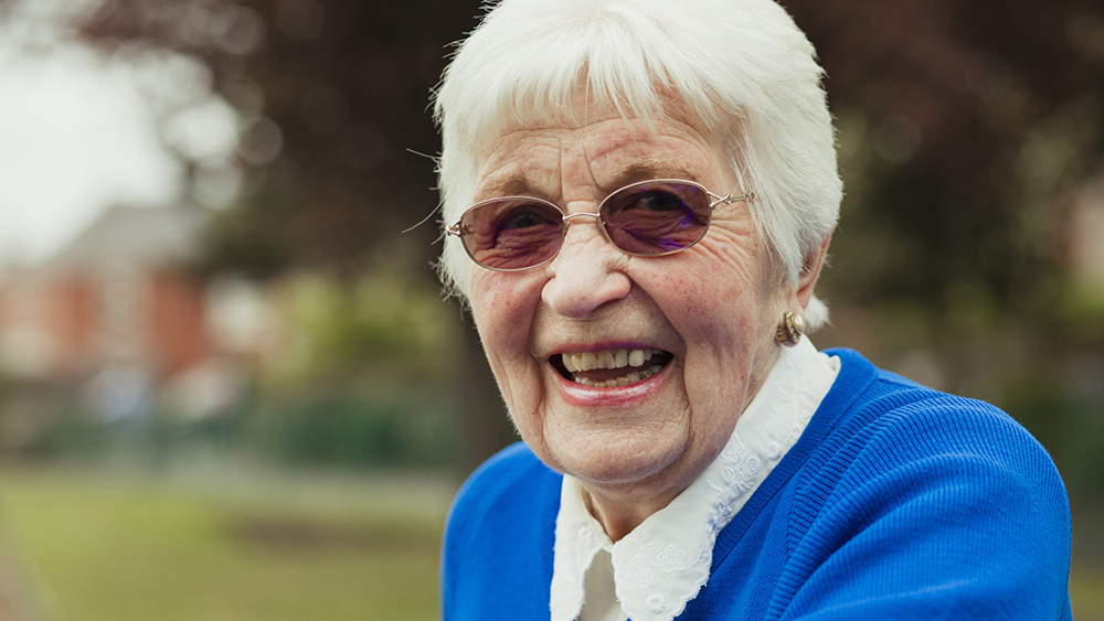 An elderly lady wearing photochromic glasses smiling for the camera.