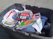 A tied, clear bag of e-cigarettes placed on top of recycling in a black recycling box.