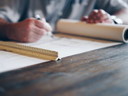 A planner using a pen and ruler whilst looking at a scroll of development plans.