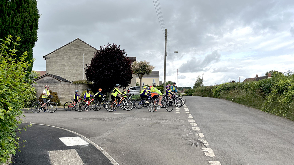 Bikeability instructors with a class of children riding bicycles, stopped at a junction.