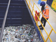 An employee in orange hi-vis and blue hard hat stands on a balcony overlooking a container full of plastic collected for recycling.