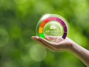 A hand holds a transparent gauge showing "CO₂ AIR QUALITY GOOD" with 0 PPM, set against a blurred green outdoor background.