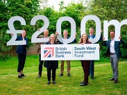 Seven people holding signs reading '£200m' and 'British Business Bank South West Investment Fund' on grass.