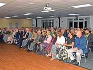 Unsung Community Hero award winners wait to receive their certificates, seated in a hall.