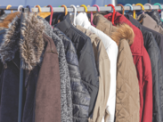 A row of winter jackets, including brown, white, red, and blue colors, hanging on a metal rack outdoors.