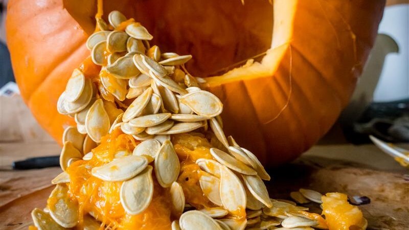 Close-up of a carved pumpkin with seeds and pulp spilling out onto a wooden surface.