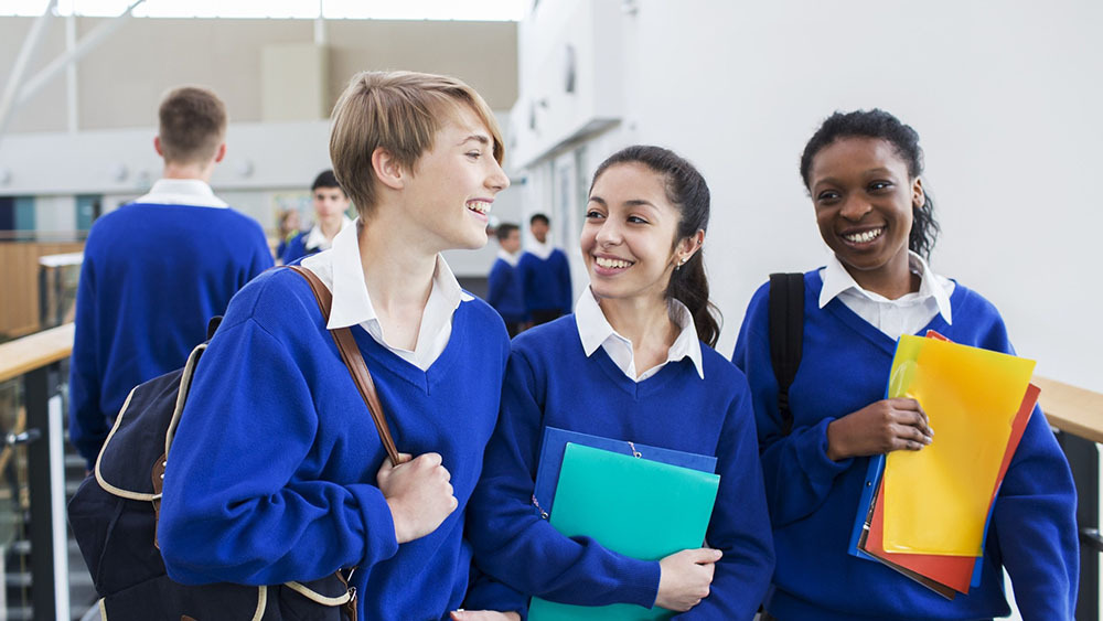 Secondary school children holding in blue uniforms, holding their bags and school files.