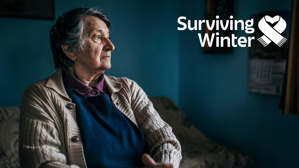 Person in a warm sweater sitting indoors with Surviving Winter appeal logo, highlighting support for older people during cold months.