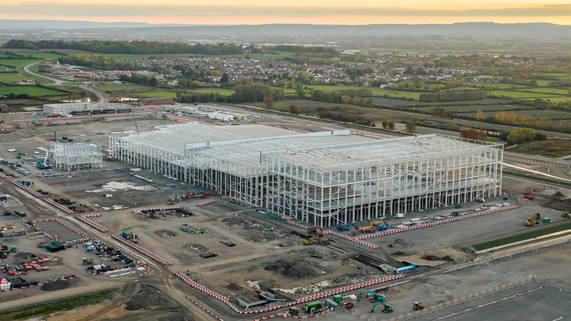 Aerial view of Agratas’ Somerset battery facility under construction, showing steel framework and surrounding countryside at sunset.