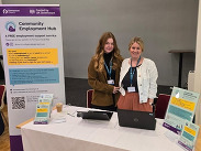 Community Employment Hub staff at an information stand with laptops and support materials promoting free employment services.