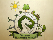 Somerset Sustainable Futures logo featuring a white dragon inside a green globe with trees, wind turbines and a sun symbol.