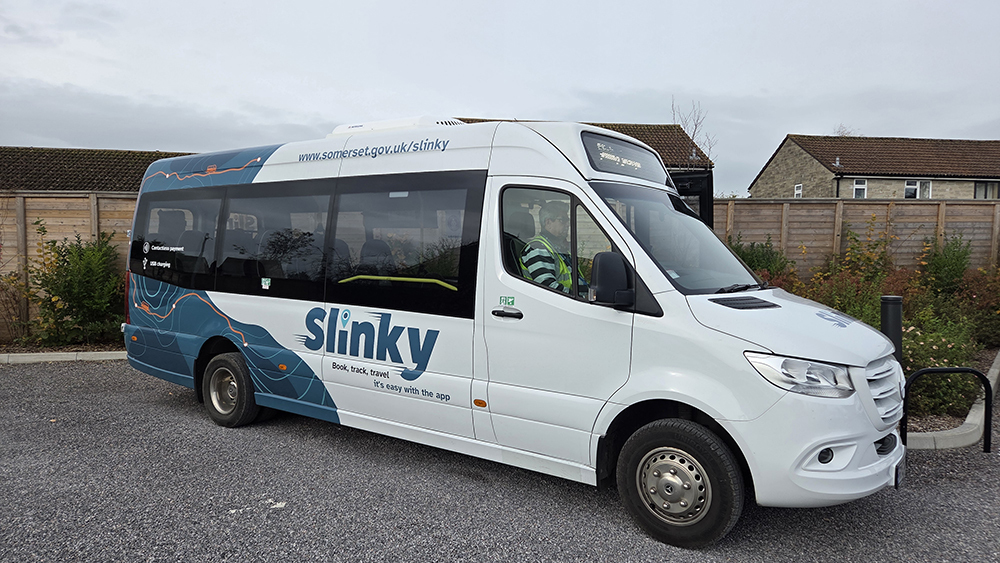 White Slinky on-demand minibus parked in Somerset promoting digital booking as service surpasses 10,000 journeys milestone