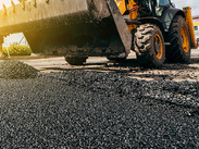Close-up of fresh asphalt being laid with a yellow road construction vehicle during resurfacing work.