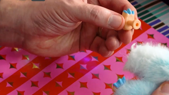 Hands inspecting a small toy part for safety against a festive wrapping paper background, highlighting Christmas toy checks.