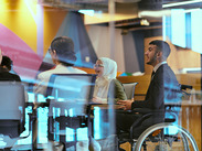 In a modern glass startup office, a wheelchair-bound director leads a successful meeting with colleagues, embodying inclusivity & teamwork.