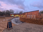 Ham Hill’s new visitor centre with wooden exterior, stone walls, and sign announcing the Lime Kiln Café is now open at dusk.