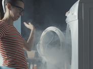 Upset woman staring at her broken washing machine, the room is full of smoke.