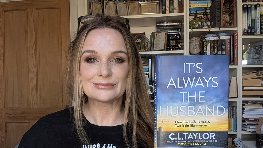 Author, CL Taylor, holding up a copy of her book titled: 'Its Always the husband'.