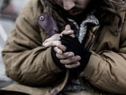 A homeless person wearing mittens rubbing their hands together in the cold.