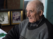 Person in a grey patterned jumper sitting indoors near framed family photos, highlighting support for older people to stay warm this winter.