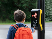 Schoolboy with backpack presses traffic light button at pedestrian crossing on way to school.