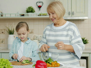 An adult and child preparing fresh vegetables together in a kitchen, chopping produce and mixing ingredients at the counter.