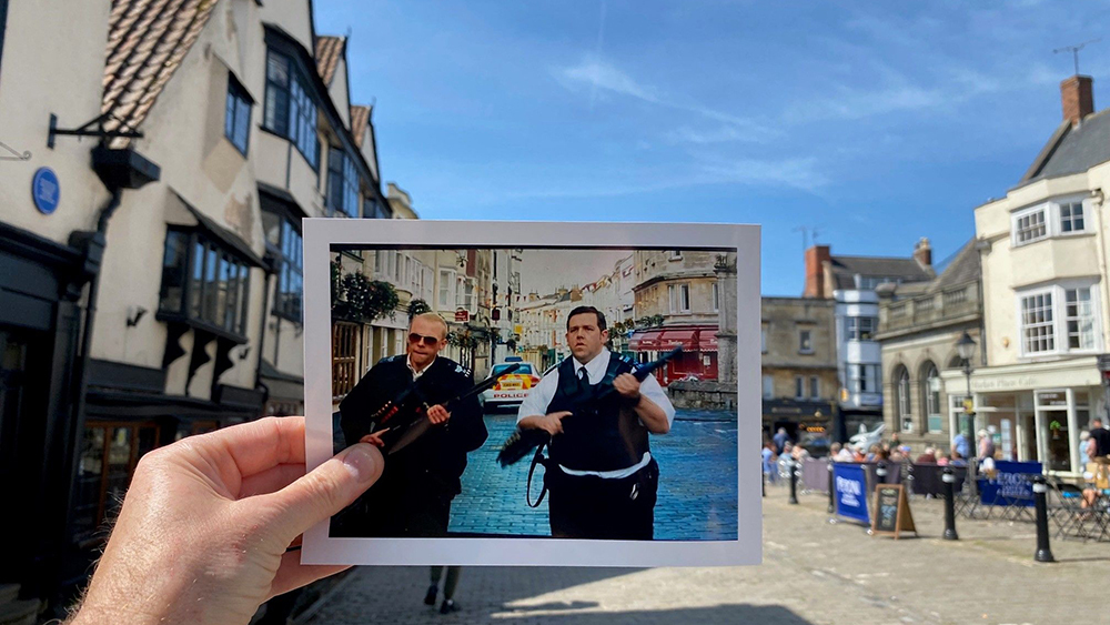 A hand holds a polaroid of a ‘Hot Fuzz’ scene against the real-life backdrop of Wells town square on a sunny day.