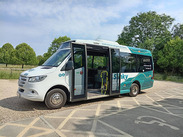 A Slinky community transport minibus parked with its door open in a rural car park on a sunny day.