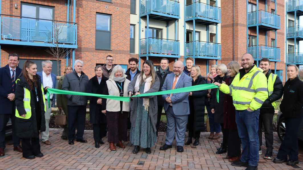 A ribbon-cutting ceremony marking the completion of new eco homes in Minehead, with officials gathered in front of the housing development.