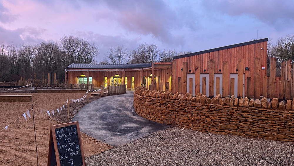 Ham Hill’s new visitor centre with wooden exterior, stone walls, and sign announcing the Lime Kiln Café is now open at dusk.