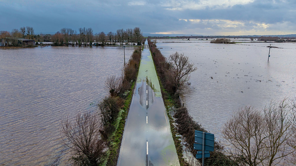 Aerial view of flooded Somerset Levels with a submerged road and surrounding fields, illustrating the impact of flooding, by Somerset By Drone.