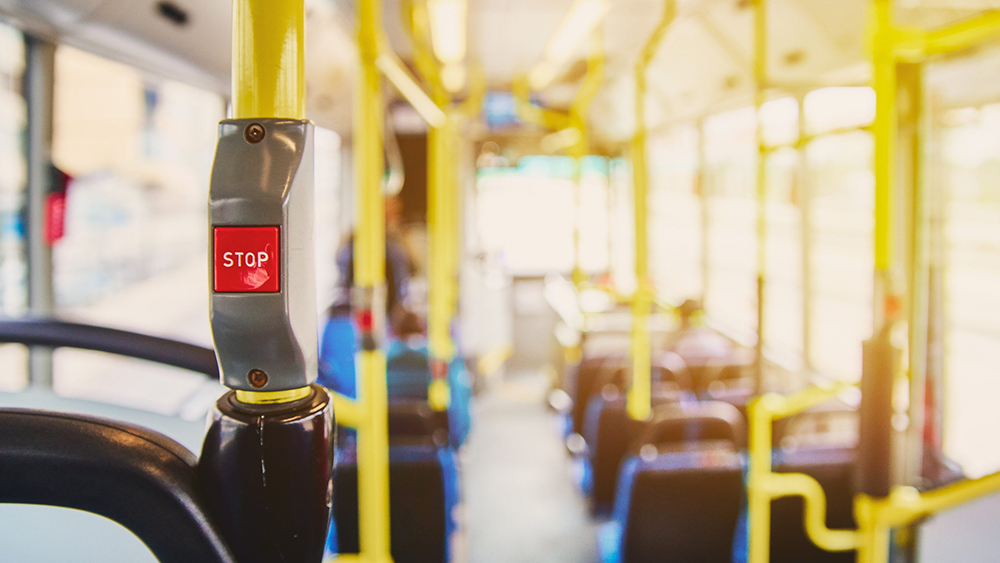 Interior of a bus showing a red STOP button, yellow handrails and blue seats, with sunlight creating a lens glare through the windows.