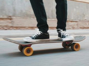 Close-up of a person wearing black trainers standing on a skateboard as it rolls along a smooth concrete surface.